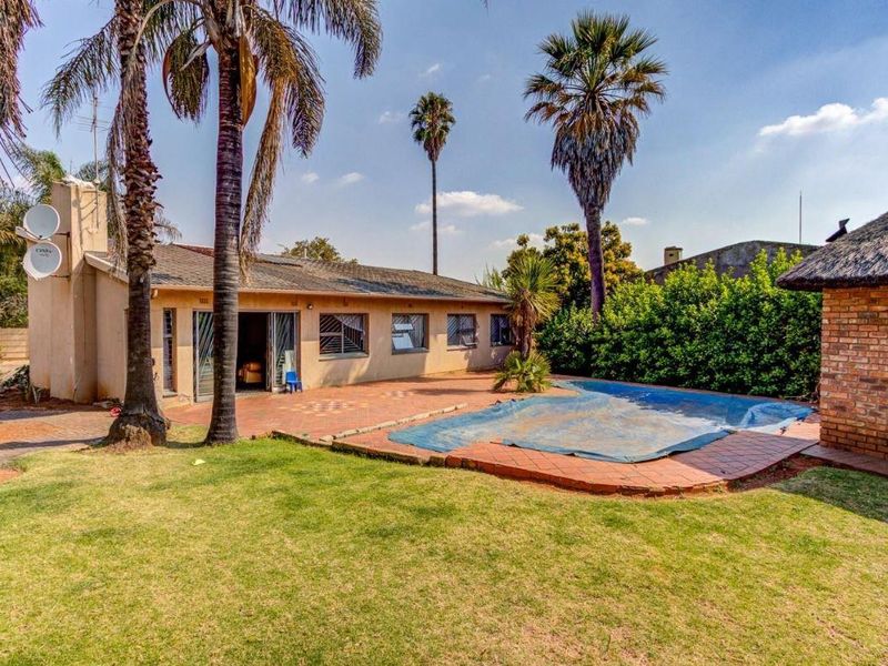 Rear exterior view featuring a swimming pool with cover, paved patio area, and a separate brick structure with a thatched roof.