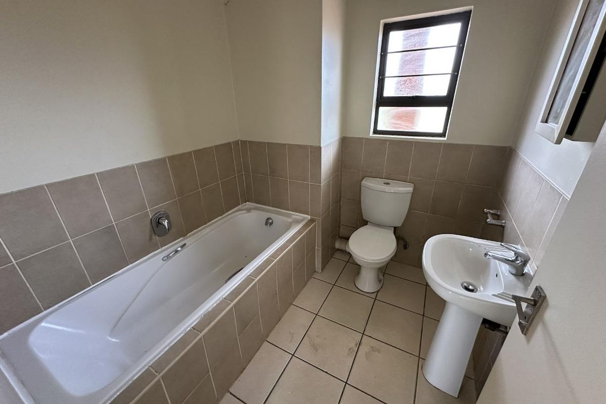 A functional bathroom featuring a built-in bathtub, pedestal basin, and toilet with neutral wall and floor tiling.