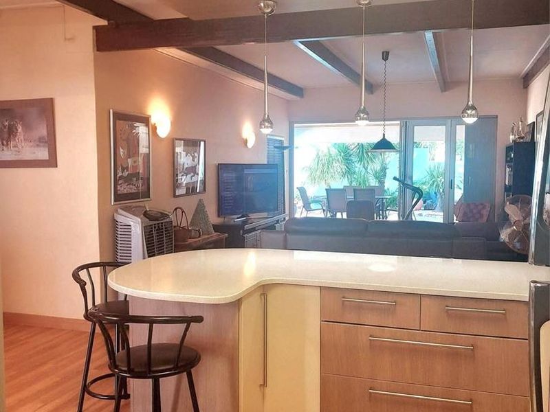 Open plan kitchen and living area featuring a central island with stone countertops, exposed timber ceiling beams, and direct access to the outdoor patio.