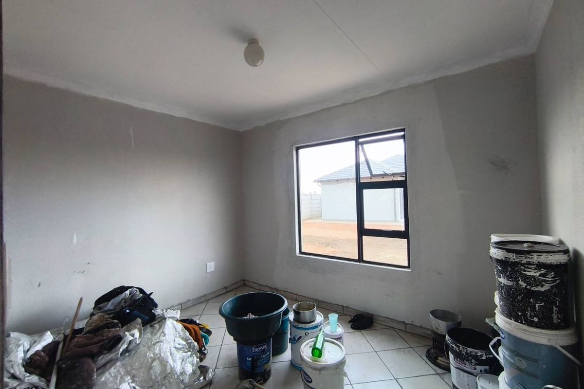 A vacant bedroom featuring tiled flooring and a window, currently undergoing interior painting and finishing work.