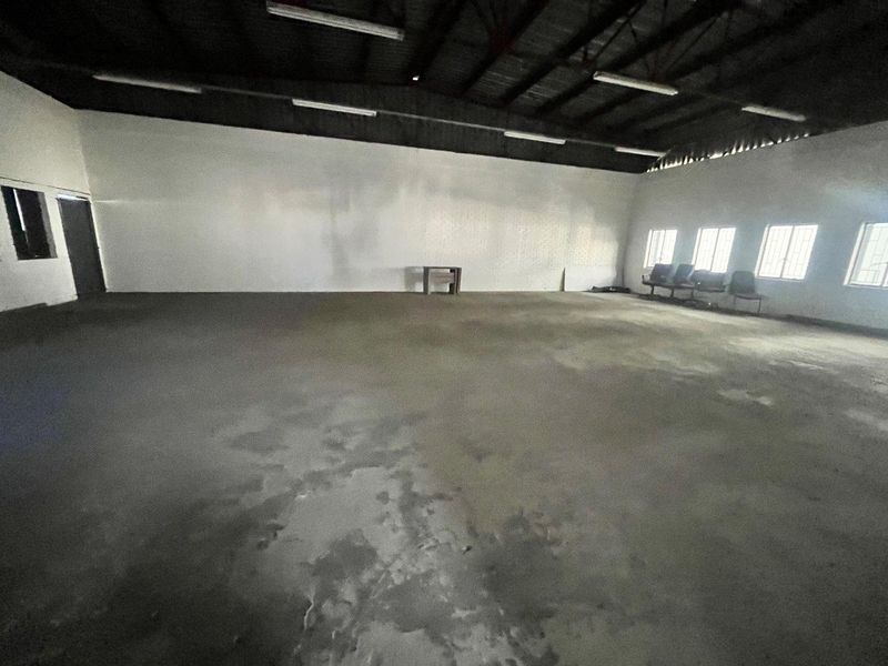 Spacious industrial utility area featuring exposed ceiling trusses, concrete flooring, and ample natural light through multiple windows.