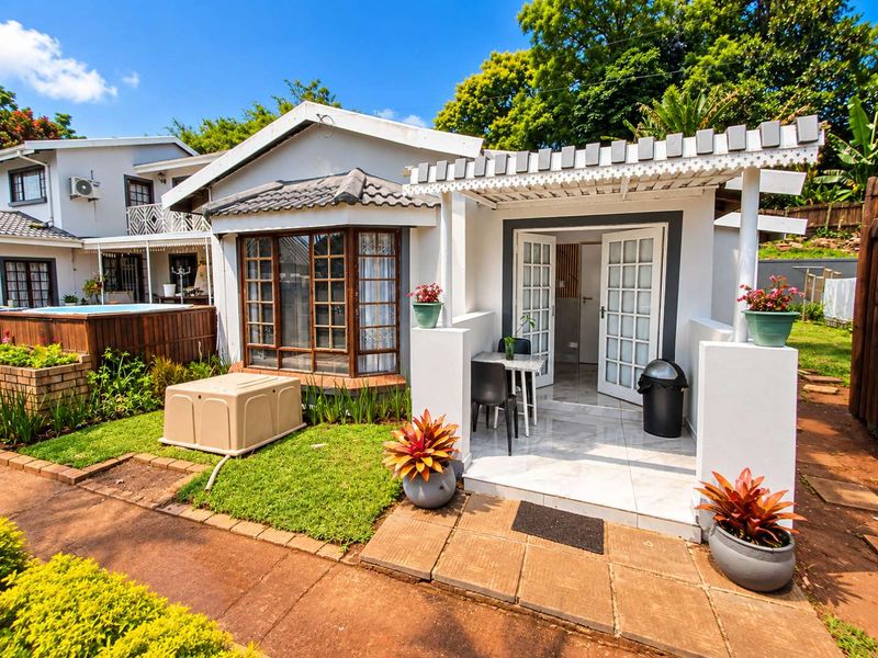 A well-maintained rear exterior view featuring a tiled patio with a pergola, french doors, and a charming bay window overlooking a landscaped garden area.