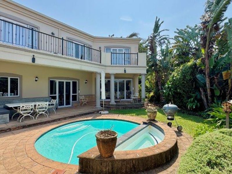 Rear exterior view featuring a swimming pool, paved patio area, and a two-story townhouse facade with a balcony and sliding glass doors.