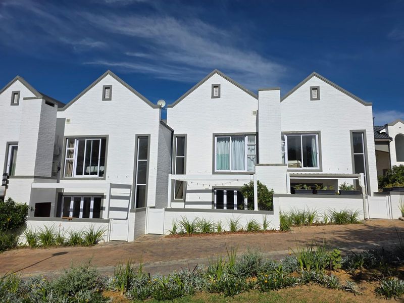 Front elevation of a modern townhouse complex featuring white brick facades, gabled rooflines, and paved driveway access.