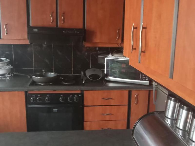 A functional kitchen featuring wood-finish cabinetry, dark countertops, a built-in oven, and a tiled backsplash, offering a practical layout for daily cooking.