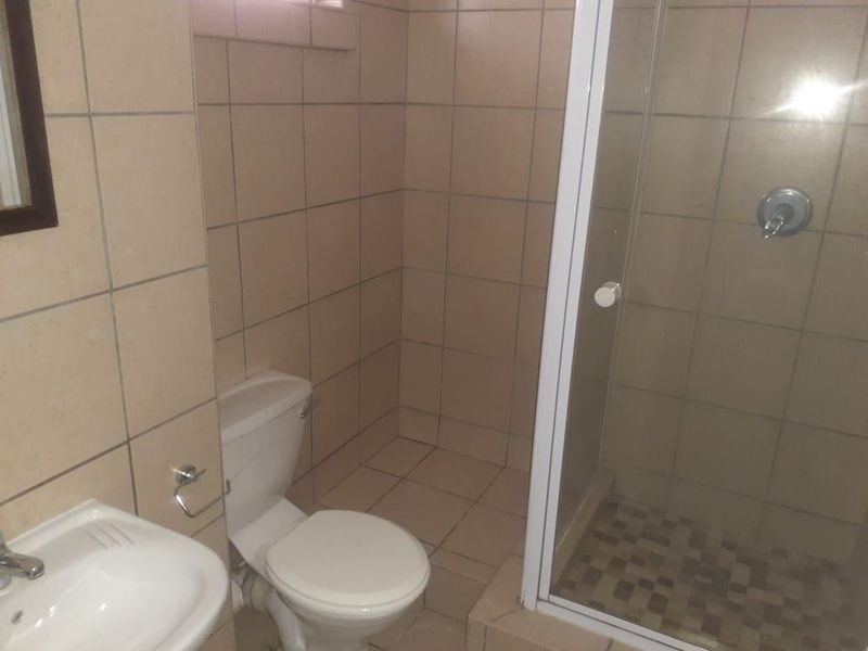 A functional bathroom featuring a shower enclosure, toilet, and pedestal basin with neutral wall and floor tiling.