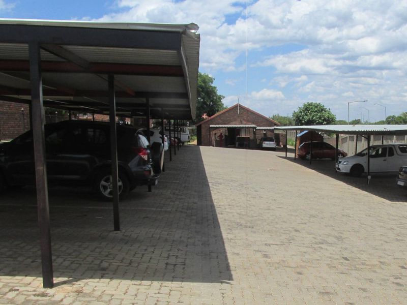 Outdoor parking area featuring multiple covered parking bays with metal roofing and a paved driveway surface.