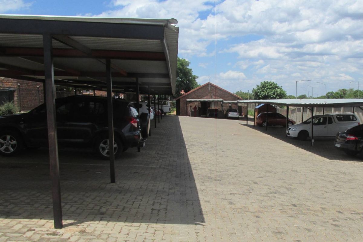 Outdoor parking area featuring multiple covered parking bays with metal roofing and a paved driveway surface.