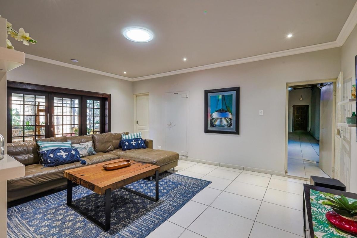 A spacious living room featuring tiled flooring, recessed ceiling lighting, a skylight, and dark-framed sliding glass doors leading to an outdoor area.