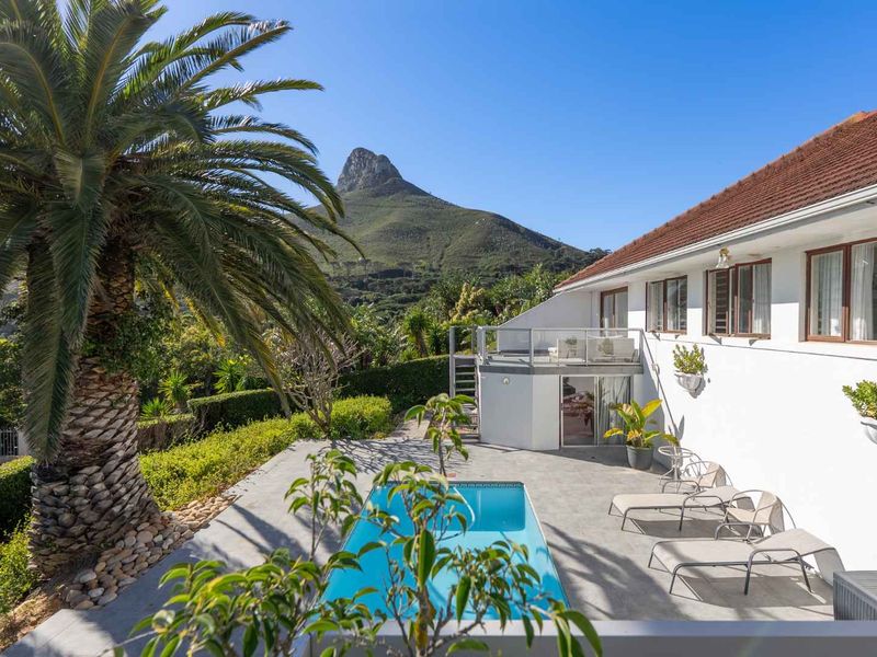 Rear exterior view featuring a swimming pool, concrete patio, raised balcony, and scenic mountain backdrop.