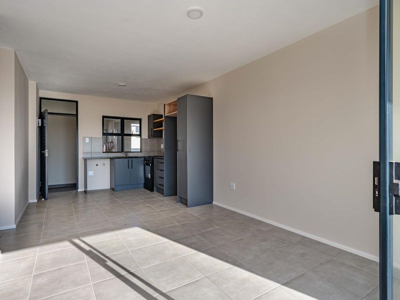 An open-plan living and kitchen area featuring modern grey cabinetry, tiled flooring, and direct access to an outdoor space through a sliding door.