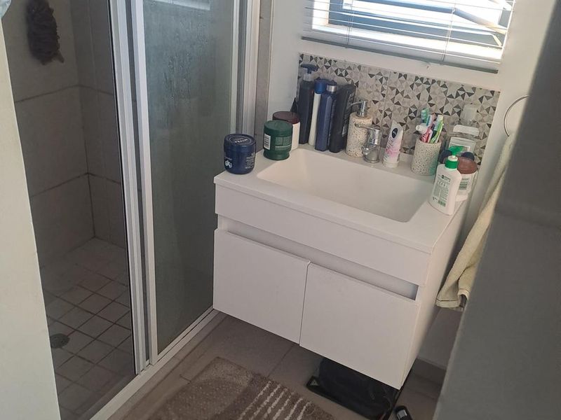 A functional bathroom featuring a modern wall-mounted vanity with basin, a glass-enclosed shower, and decorative tiled splashback.