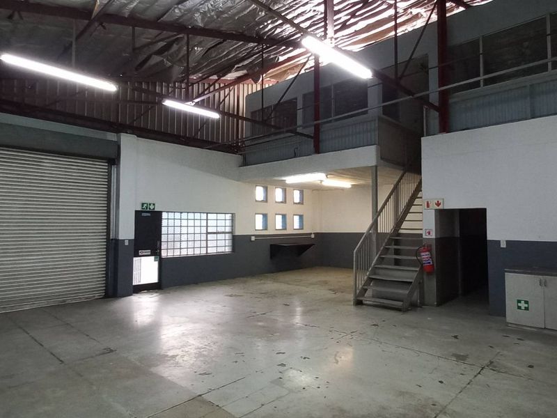 Spacious industrial utility area featuring a large roller shutter door, mezzanine level with steel staircase, and functional built-in cabinetry.