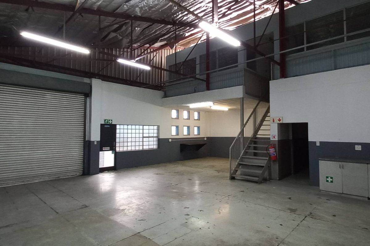 Spacious industrial utility area featuring a large roller shutter door, mezzanine level with steel staircase, and functional built-in cabinetry.