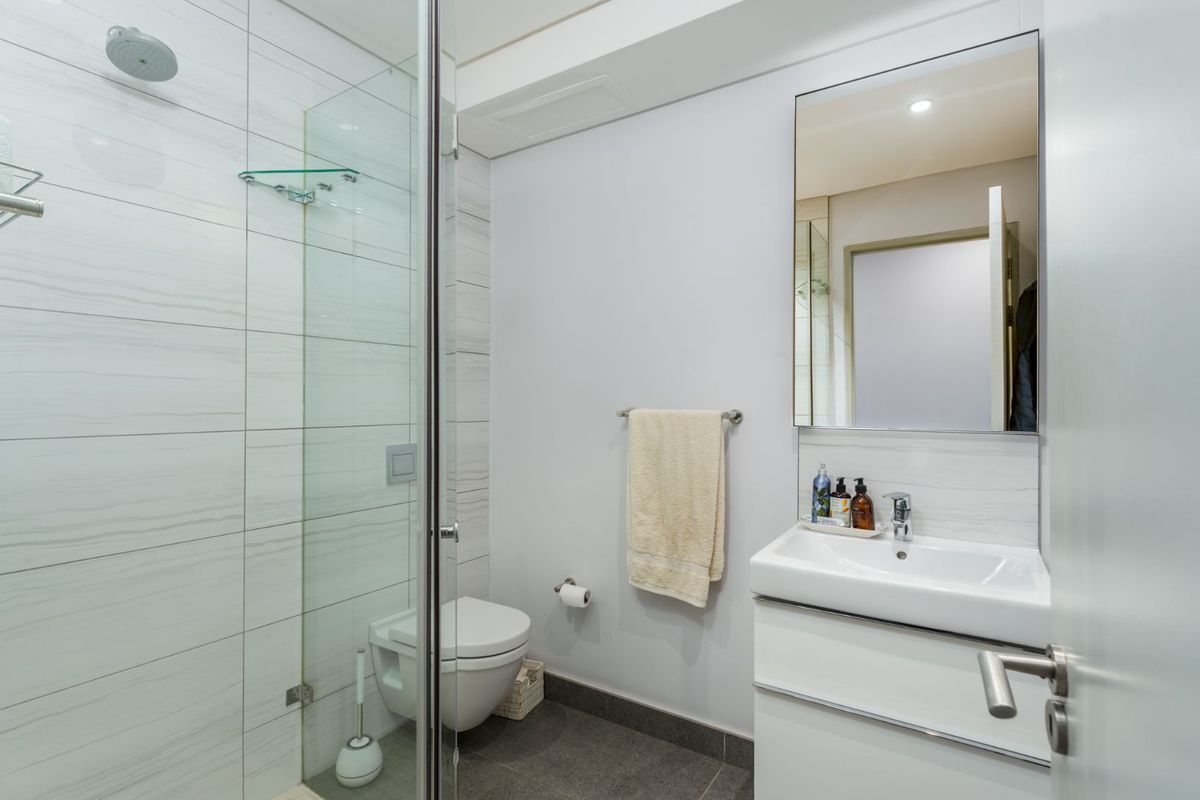 Modern bathroom featuring a glass-enclosed shower, wall-mounted toilet, and a sleek vanity basin with a wall-mounted mirror.