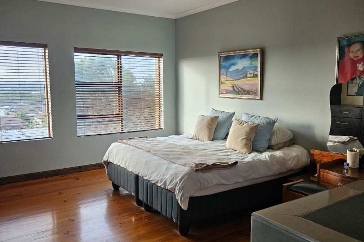 Spacious bedroom featuring polished timber flooring, large windows with venetian blinds, and neutral wall tones.