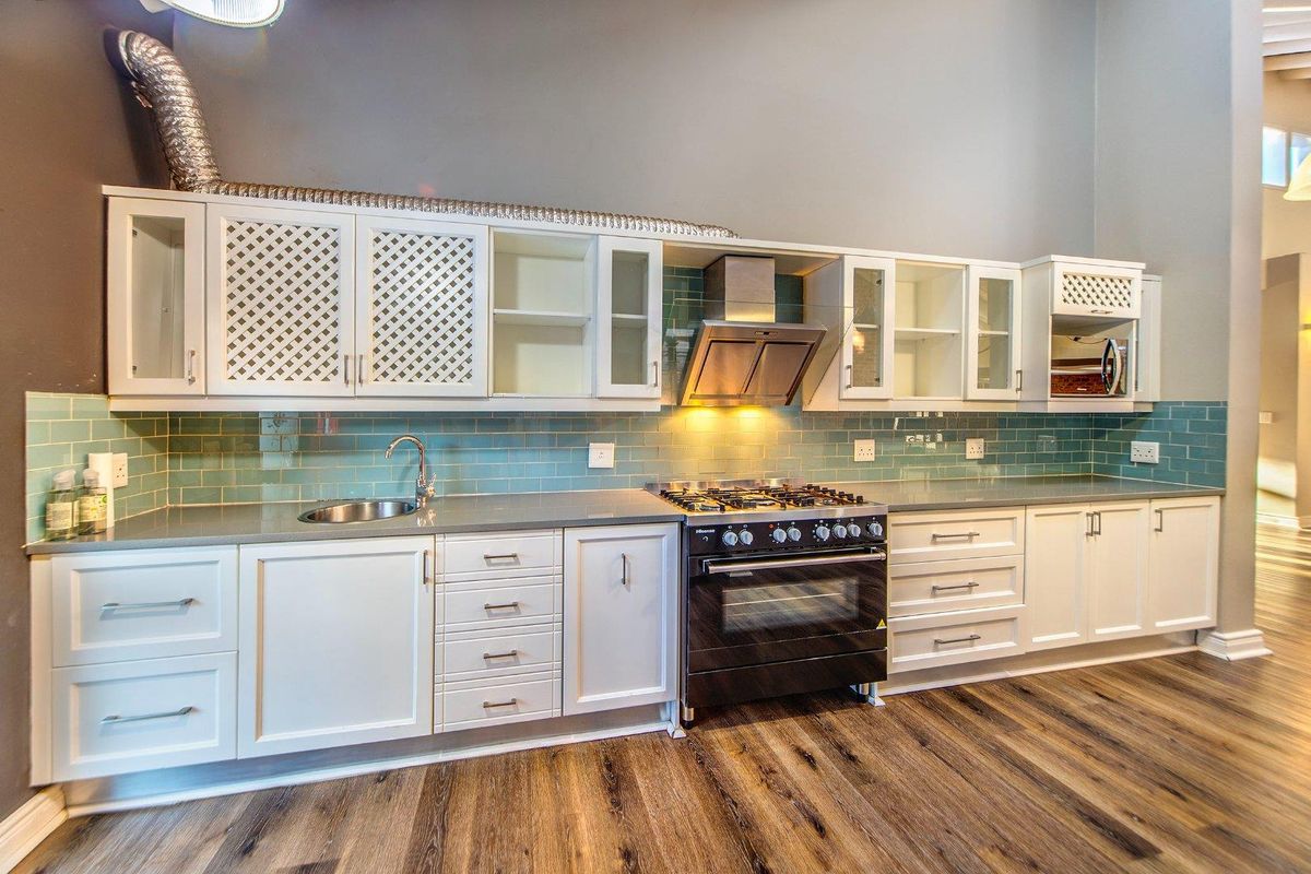 A well-appointed kitchen featuring white cabinetry, a gas stove with extractor fan, subway tile backsplash, and durable wood-look flooring.
