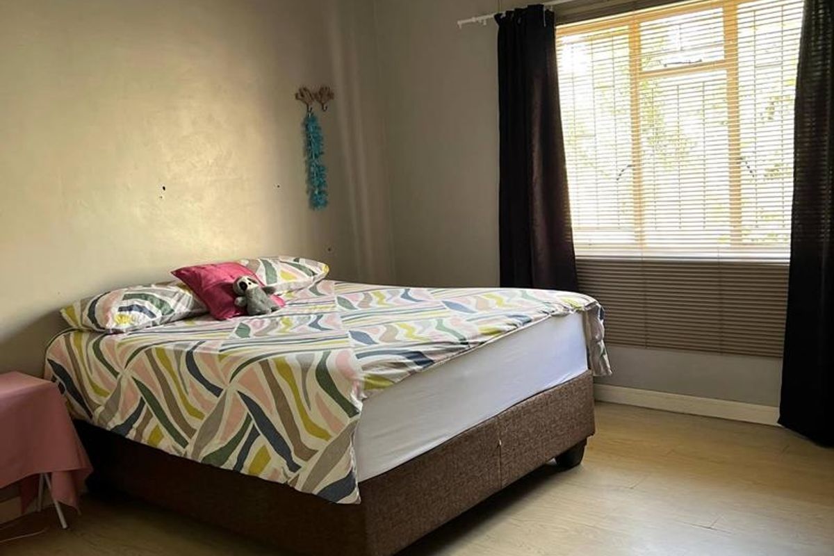 A bedroom featuring light-toned laminate flooring, neutral wall paint, and a window fitted with horizontal blinds and curtains.