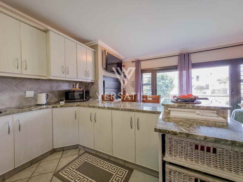 A functional kitchen featuring granite countertops, ample built-in cabinetry, and a tiled backsplash, with direct access to an outdoor area through sliding glass doors.