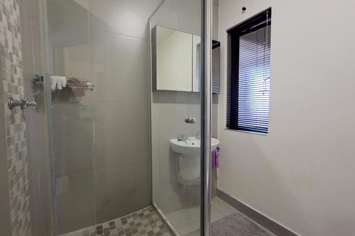 A modern bathroom featuring a glass-enclosed shower, a wall-mounted basin, and a mirrored medicine cabinet with tiled accents.