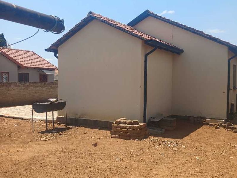 Rear view of the house showing the exterior wall, tiled roof, and gutter system with an unfinished garden area.