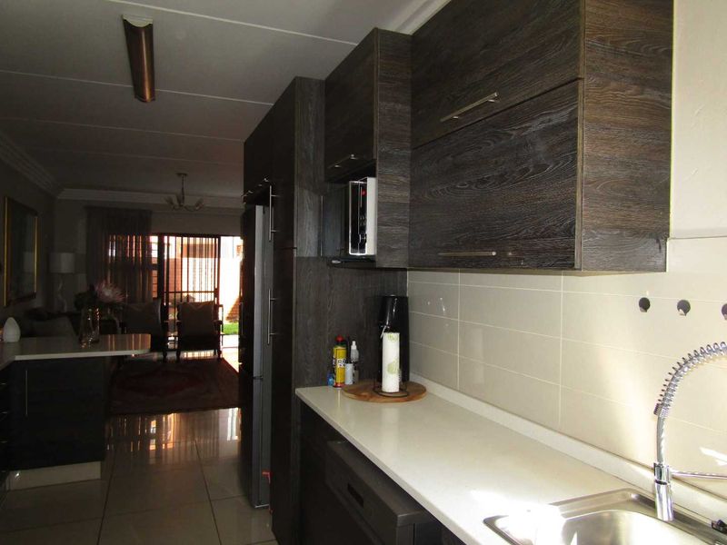 Open plan kitchen featuring dark wood cabinetry, stone countertops, and a tiled backsplash, flowing into the adjacent living area with tiled flooring.