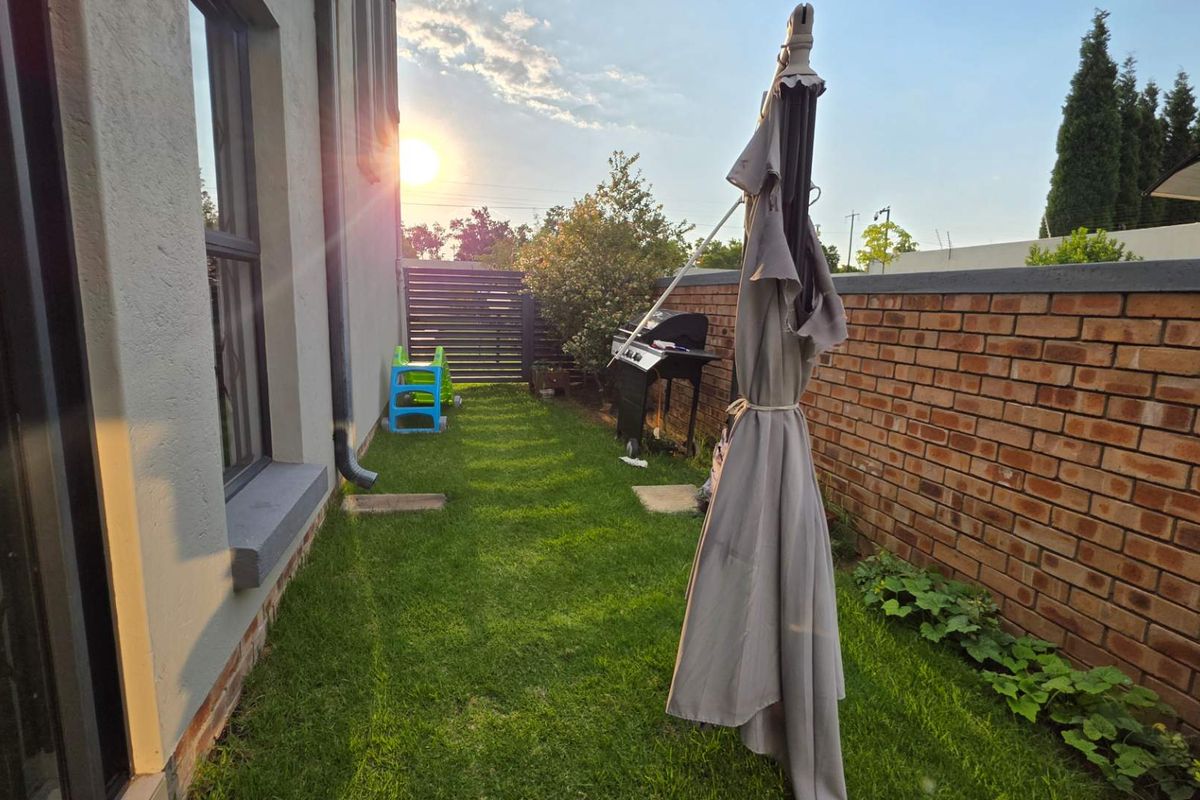 A private rear garden area featuring a brick boundary wall, lawn, and direct access to the townhouse interior through large sliding glass doors.