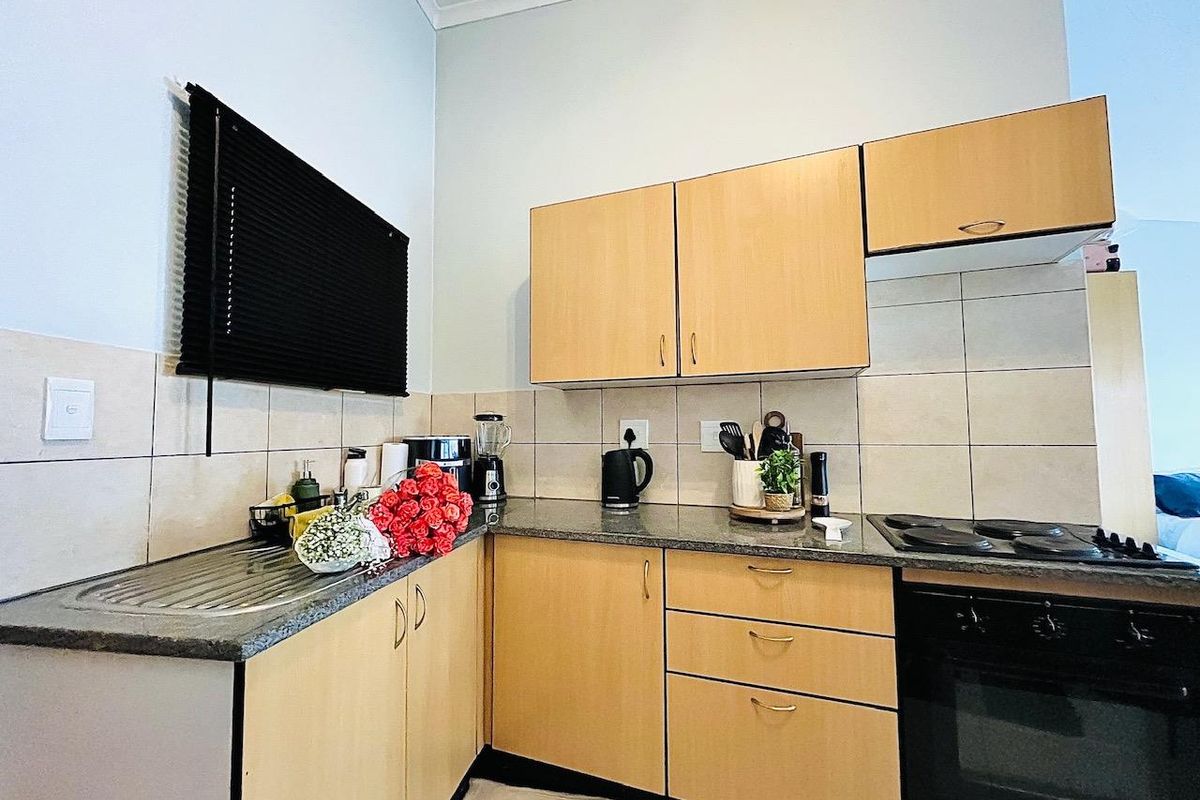 Compact kitchen featuring light wood-finish cabinetry, granite countertops, tiled backsplash, and integrated oven and hob.