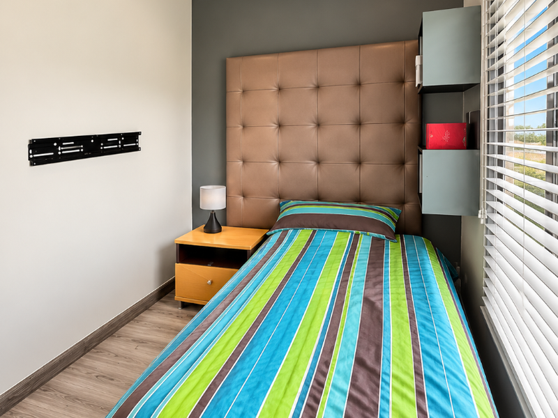 A well-maintained bedroom featuring laminate flooring, recessed downlights, crown molding, and built-in shelving, with a wall-mounted bracket for television installation.