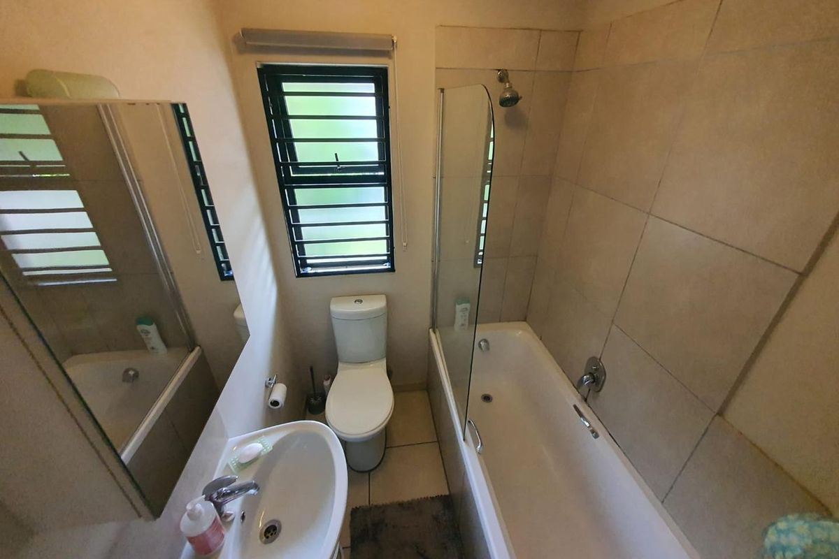 A functional bathroom featuring a bathtub with a glass shower screen, a pedestal basin, and a toilet, finished with neutral wall tiles.