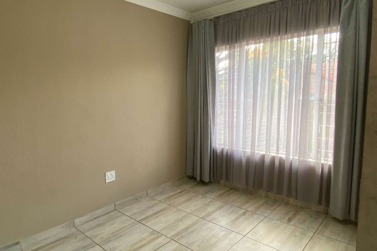 A clean, empty bedroom featuring neutral wall tones, tiled flooring, and large windows with installed curtain tracks.