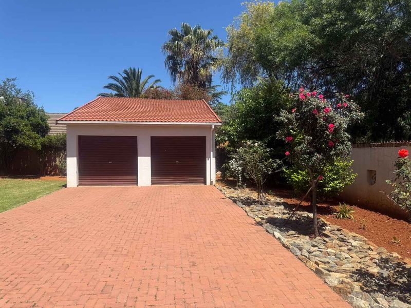 A well-maintained double garage featuring a tiled roof and a paved driveway, set within a landscaped garden with a boundary wall.