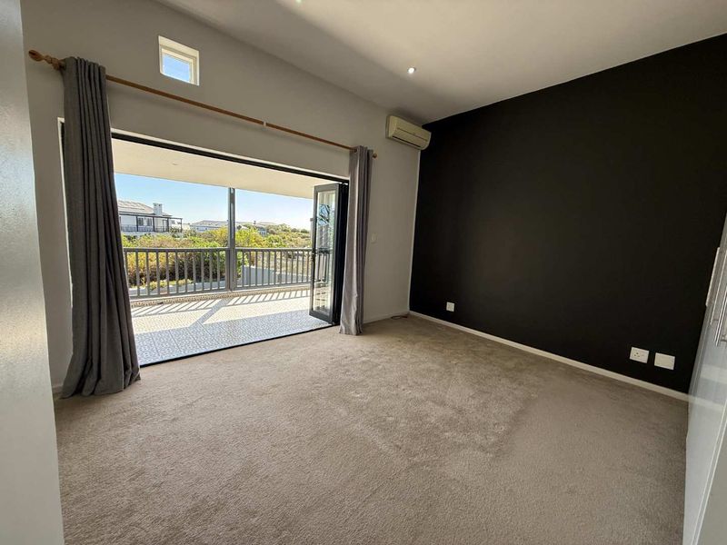 Spacious bedroom featuring neutral carpeting, a dark accent wall, air conditioning, and large bi-fold doors opening onto a private balcony.