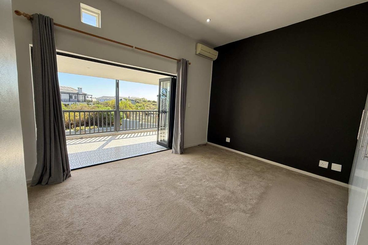 Spacious bedroom featuring neutral carpeting, a dark accent wall, air conditioning, and large bi-fold doors opening onto a private balcony.
