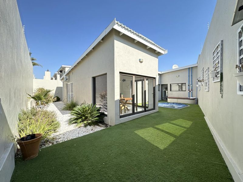 A well-maintained rear courtyard featuring artificial turf, a small plunge pool, and modern sliding glass doors providing access to the home.