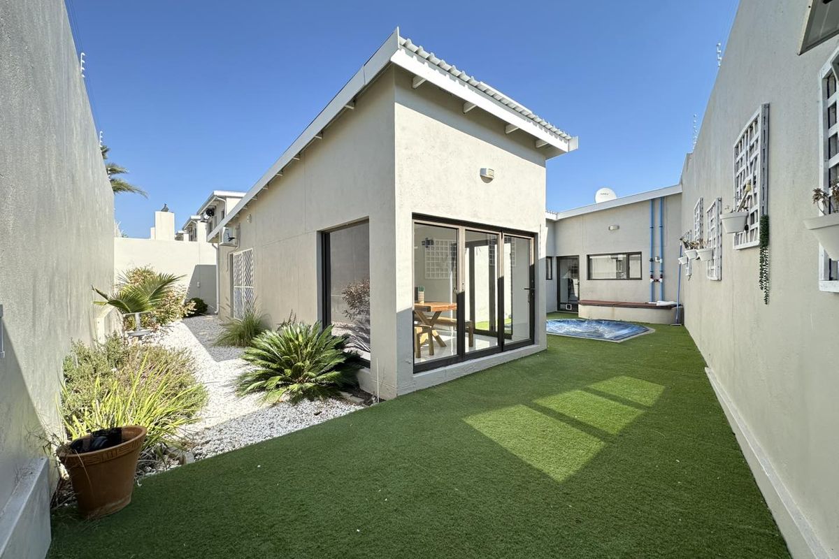 A well-maintained rear courtyard featuring artificial turf, a small plunge pool, and modern sliding glass doors providing access to the home.