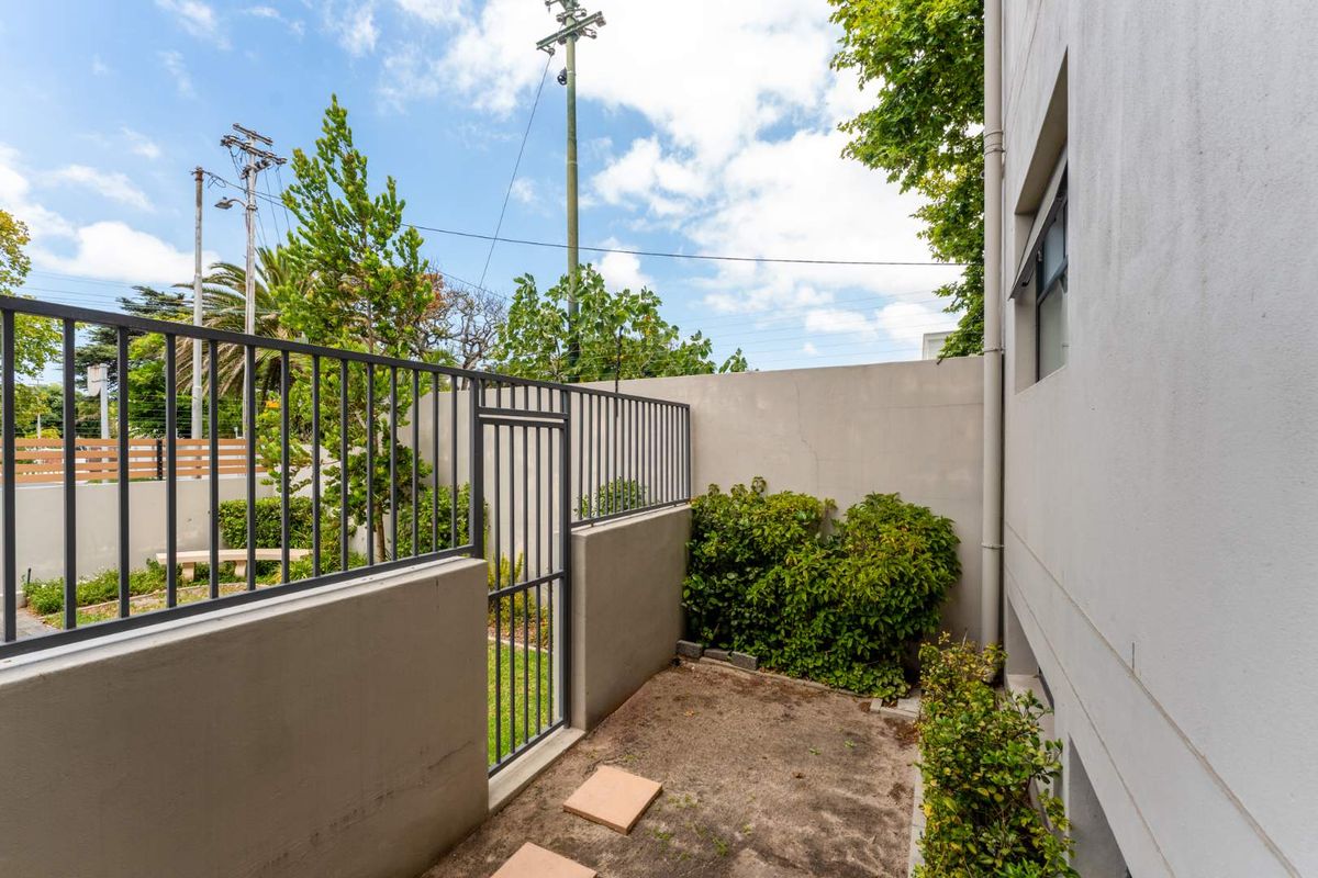 A private rear courtyard area featuring a metal security fence, gate, and boundary wall with established garden beds.