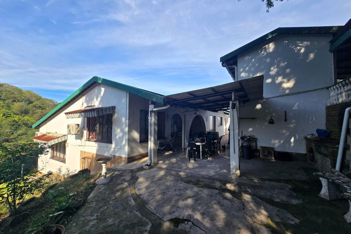 Rear exterior view of the house featuring a covered patio area, concrete paving, and established garden surroundings.