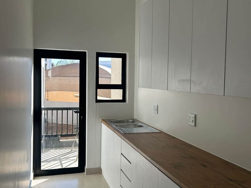 A clean and modern scullery featuring white built-in cabinetry, a wooden countertop with an integrated stainless steel sink, and direct access to an outdoor area.