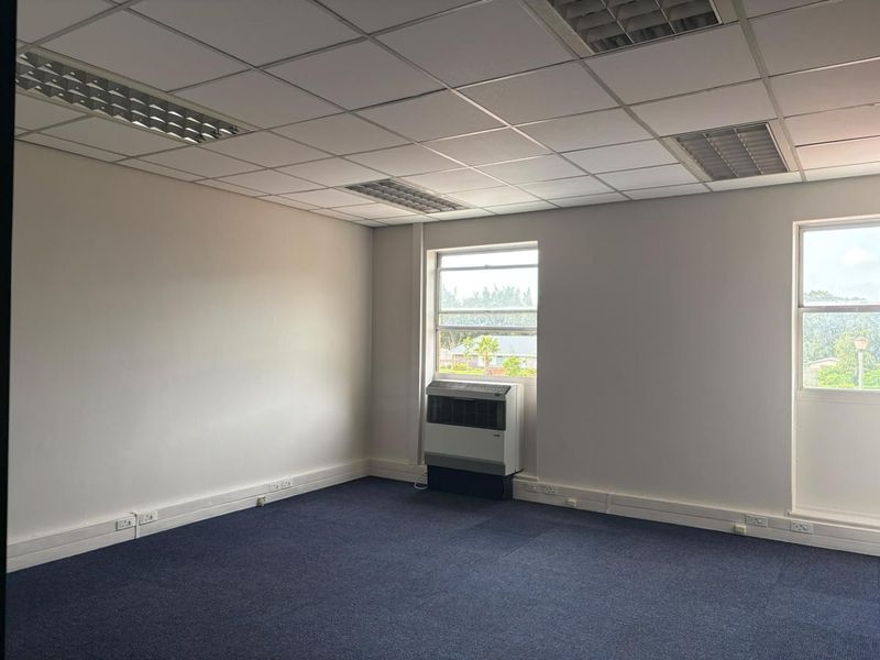 A vacant office space featuring a suspended ceiling, recessed lighting, blue carpet flooring, and a window-mounted air conditioning unit.