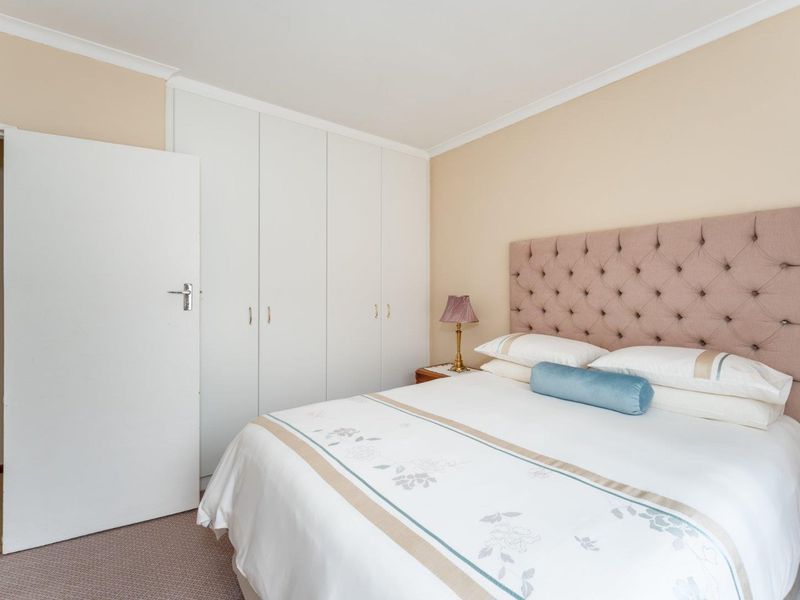 A well-maintained bedroom featuring neutral walls, carpeted flooring, and ample built-in cupboard storage, with an adjacent view into the bathroom.
