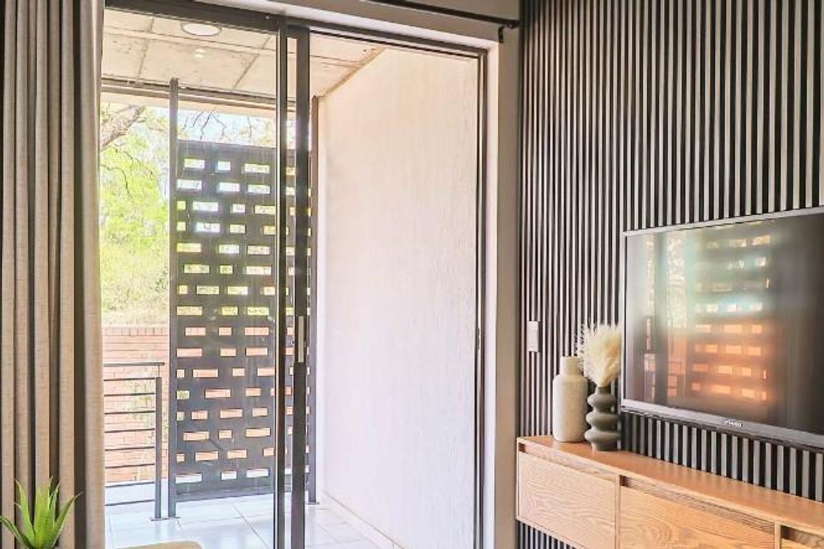 Modern living area featuring a sleek slatted feature wall, wall-mounted television, and large sliding glass doors opening onto a private balcony.