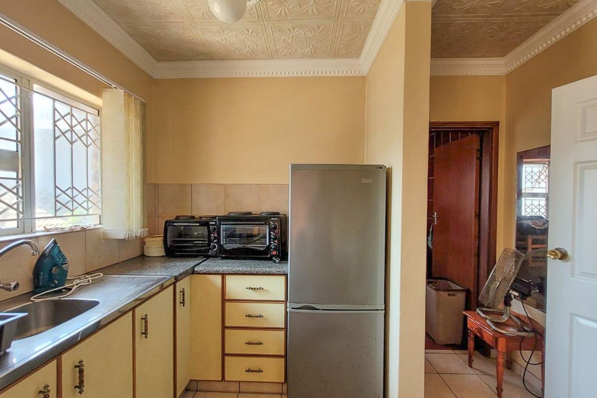 A functional kitchen featuring built-in cabinetry, a stainless steel sink, tiled splashbacks, and a decorative ceiling, providing a practical workspace.