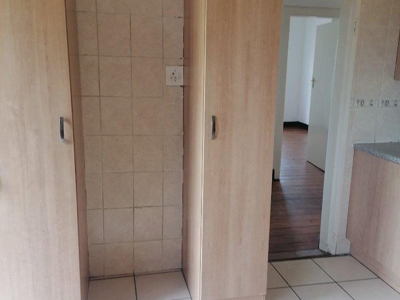A functional kitchen area featuring light wood-toned built-in cabinetry, tiled flooring, and a tiled wall splashback, with an adjacent doorway leading to another room.