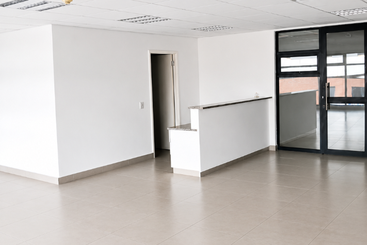 A bright, open-plan office space featuring a reception counter, tiled flooring, and a suspended ceiling with recessed lighting.