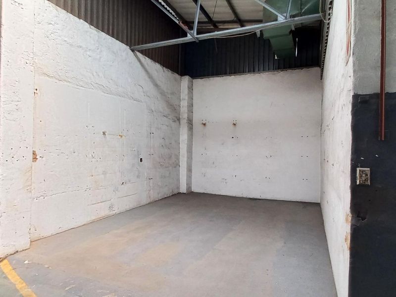 An empty industrial utility space featuring exposed steel roof trusses, concrete flooring, and painted masonry walls, suitable for storage or workshop use.