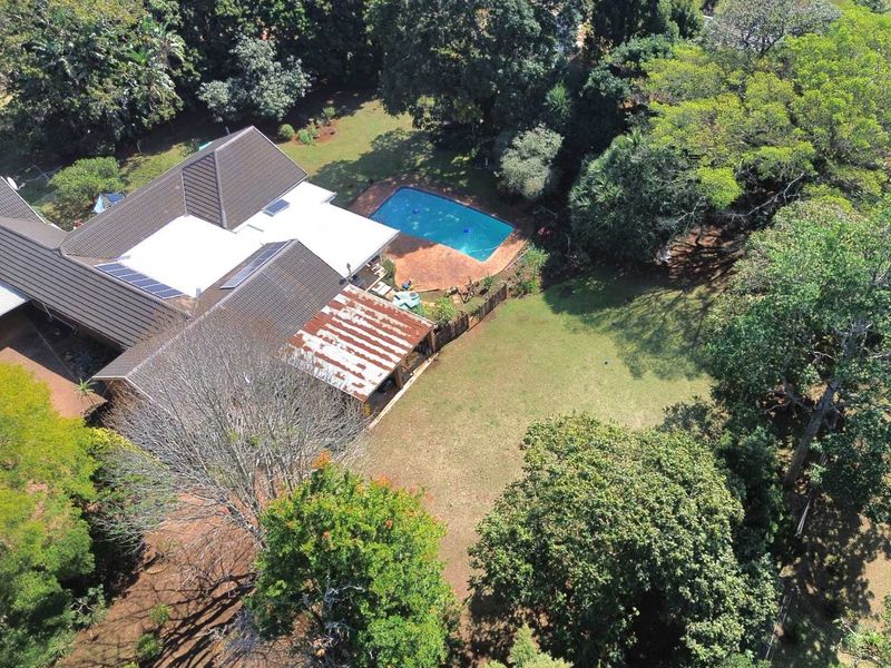 Aerial view of a residential property featuring a swimming pool, large garden, solar panels, and a patio area with weathered roofing.