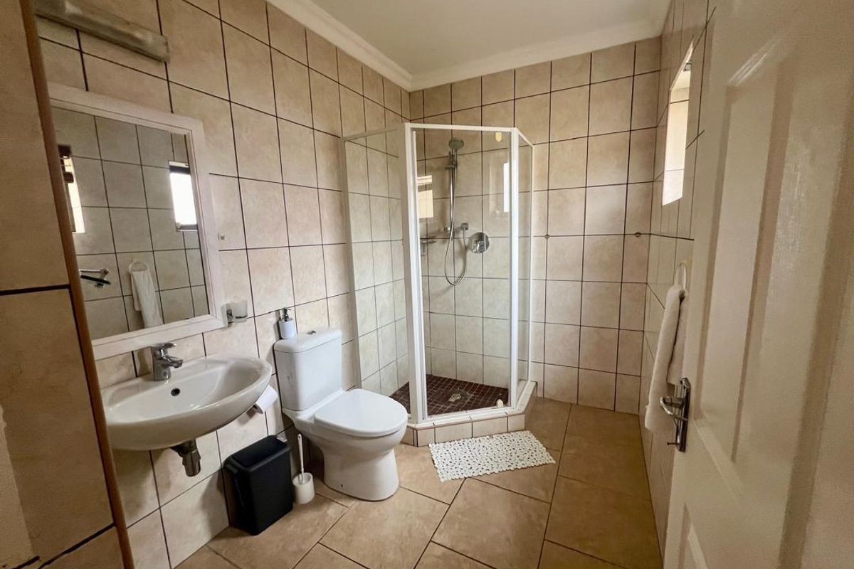 A functional bathroom featuring a corner shower enclosure, pedestal basin, and toilet with neutral floor-to-ceiling wall tiling.