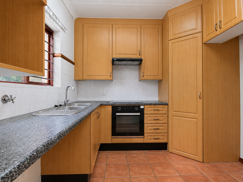 A functional kitchen featuring light wood-tone cabinetry, granite-look laminate countertops, built-in oven, electric hob, and terracotta floor tiles.