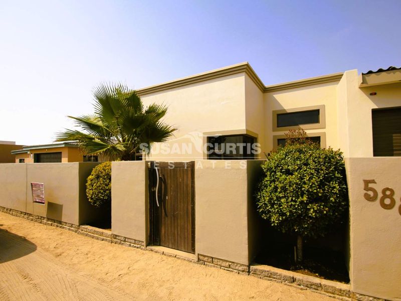 Front elevation of a modern house featuring a solid boundary wall, pedestrian gate, and clean architectural lines.
